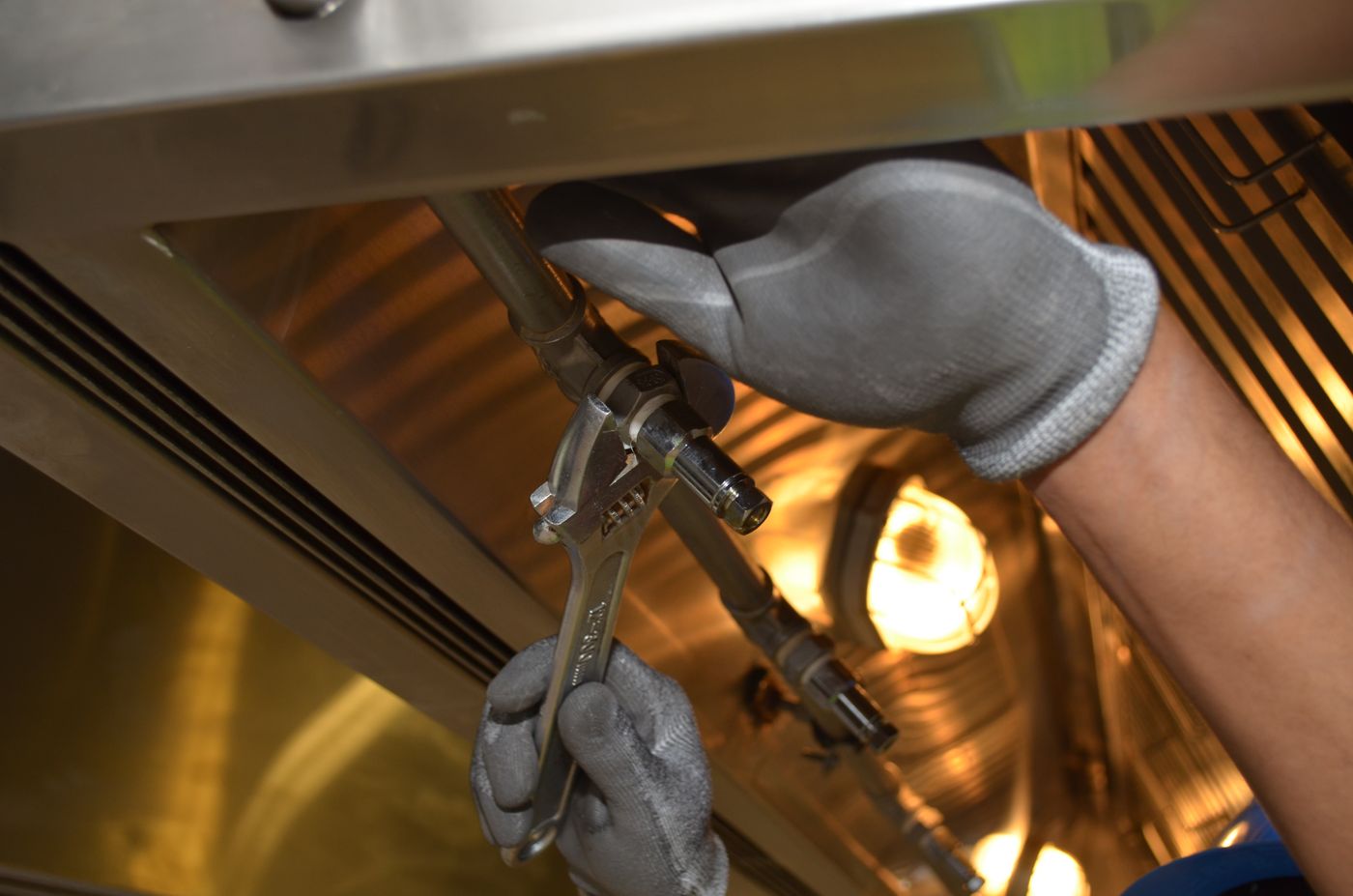 Technician repairing plumbing beneath a sink with a wrench